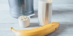 protein shake ingredients sitting on a table; a banana, protein, milk and shaker cup