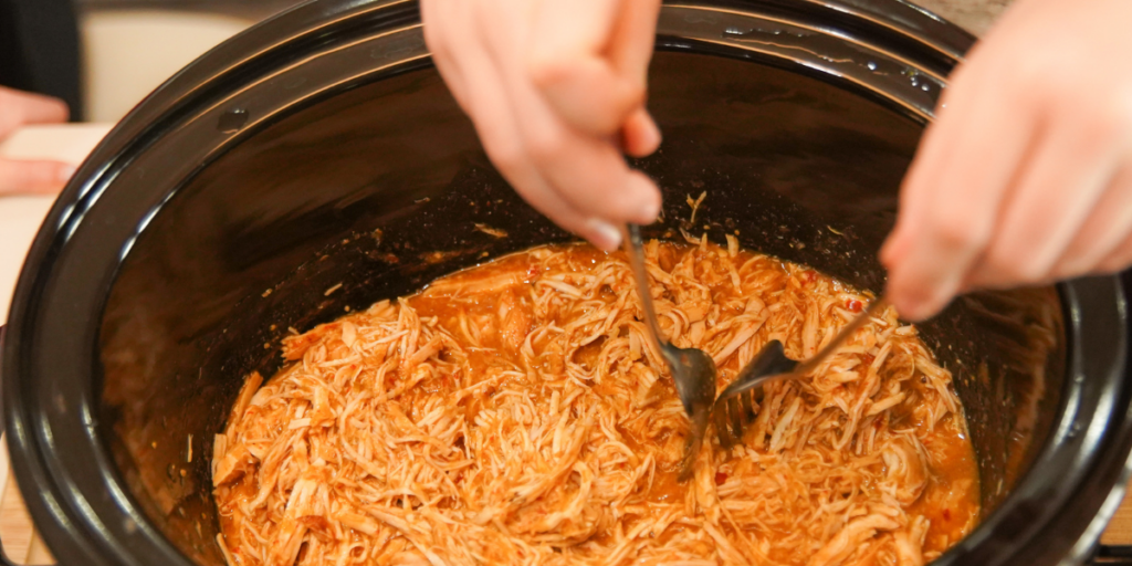 crockpot full of shredded chicken being shredded with a for demonstrating quick meals